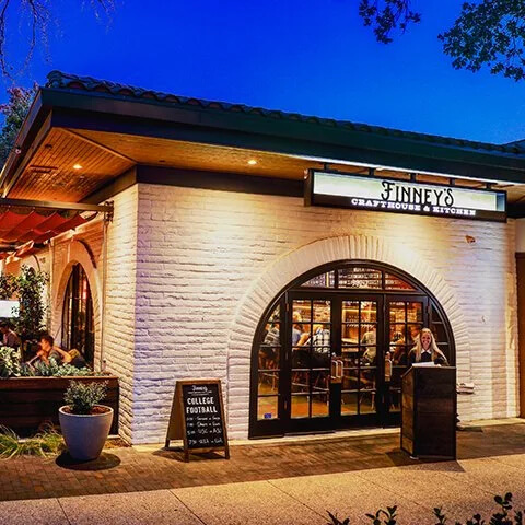 Exterior view of Finney's Craft House & Kitchen at dusk, featuring warm lighting, arched windows, and an inviting patio with diners.